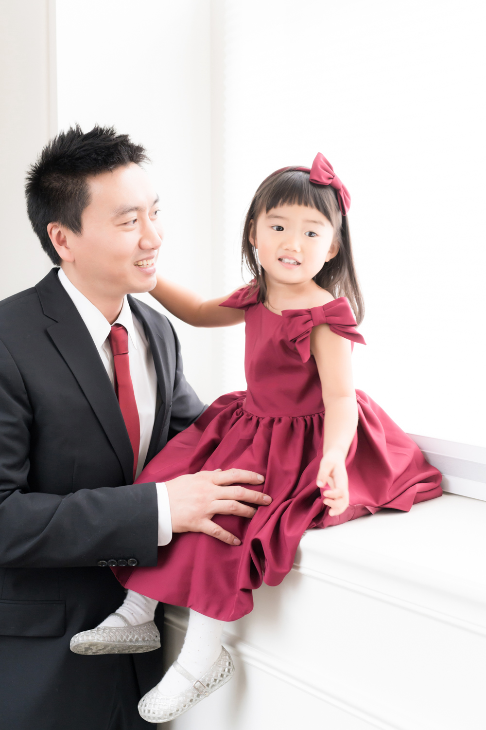 A father holds his daughter on a windowsill as she grins during a father daughter photoshoot.