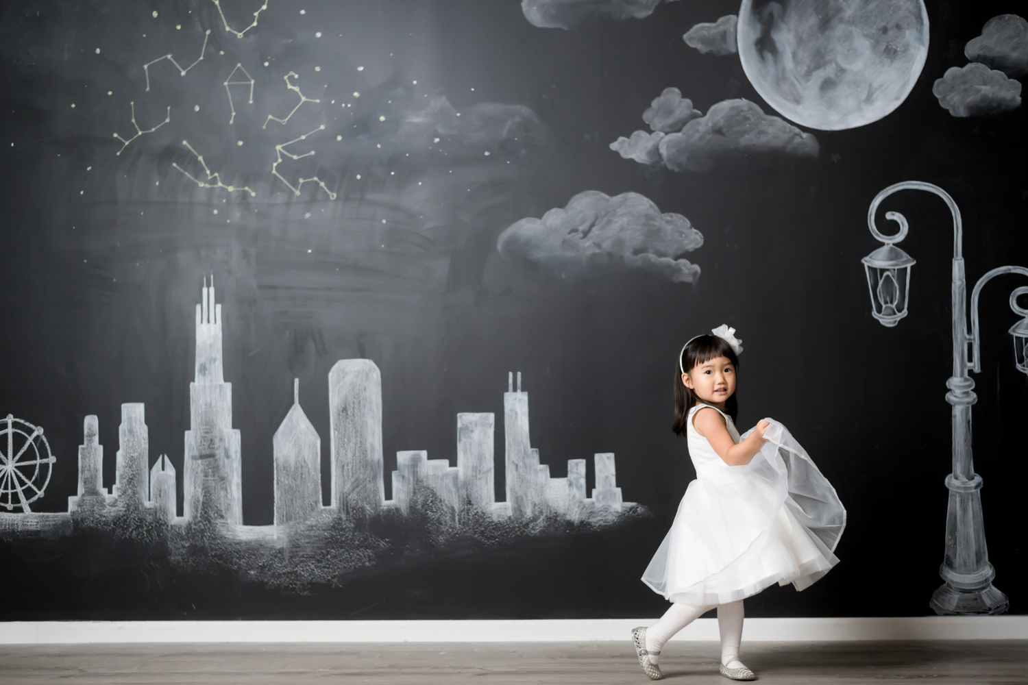 Hyorin holds her dress and dances in front of a chalk Chicago skyline mural.