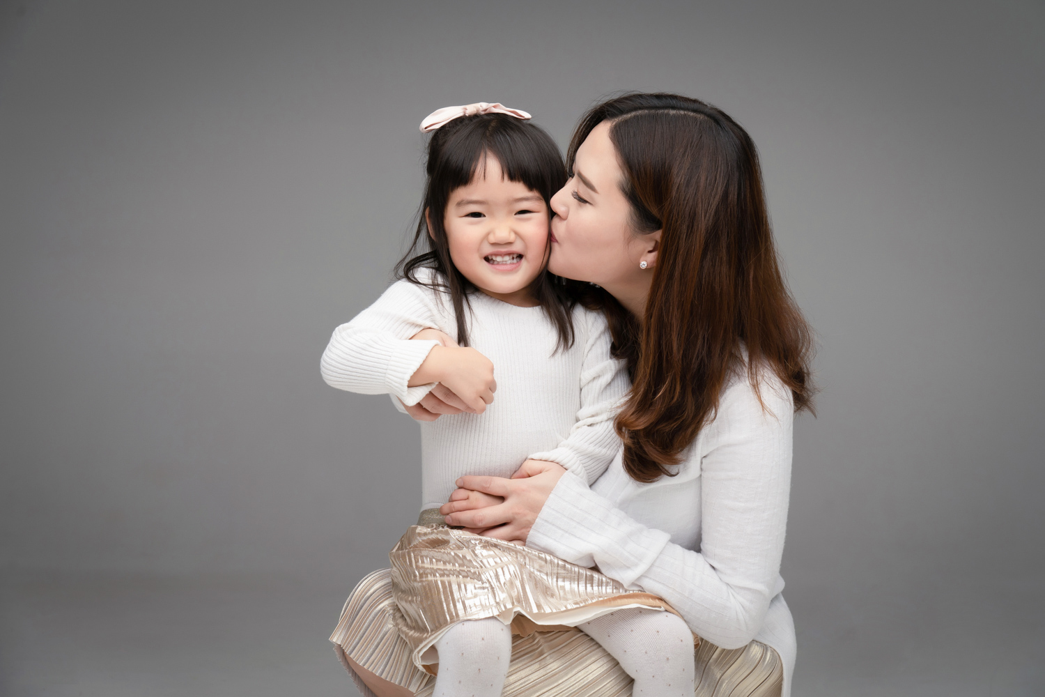 Janice kisses her daughter while holding her during a family photoshoot.