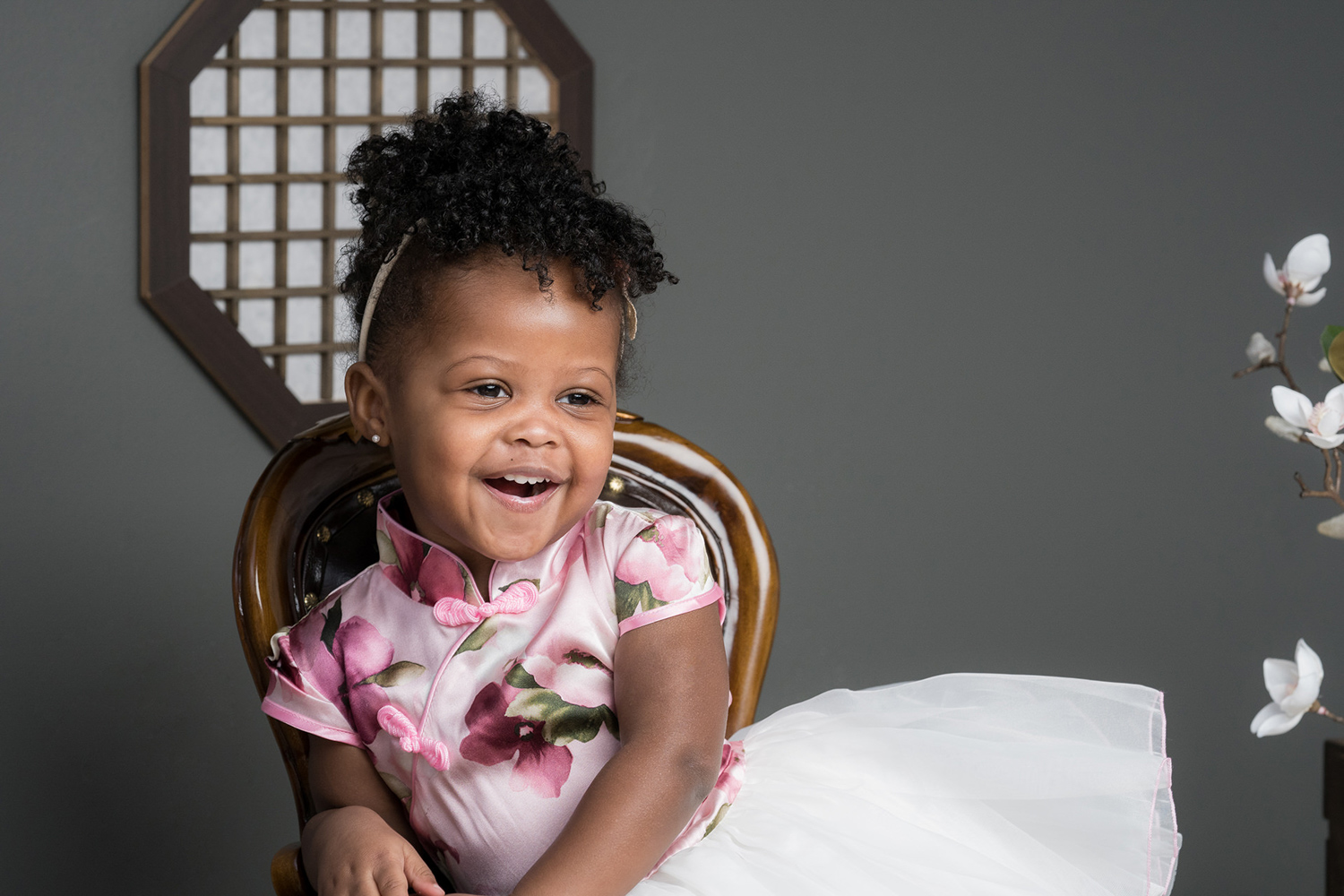 Two-year-old Sophia sits in a miniature chair and smiles during a family photoshoot.