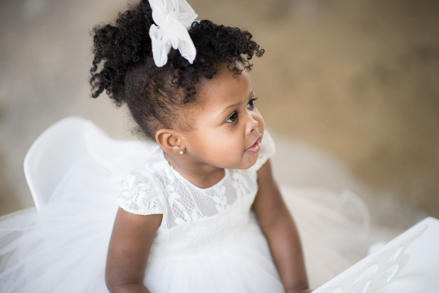 Chicago toddler sits in a white dress and looks at her parents during a photo session.